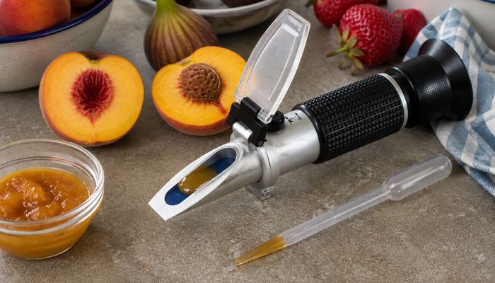 Rifrattometro con succo di frutta per misurare i gradi Brix, accanto a pesche, fichi e fragole