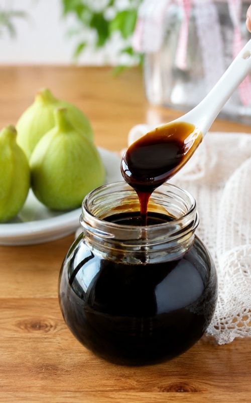 Vincotto di fichi denso che cola da un cucchiaio bianco in un vasetto di vetro
