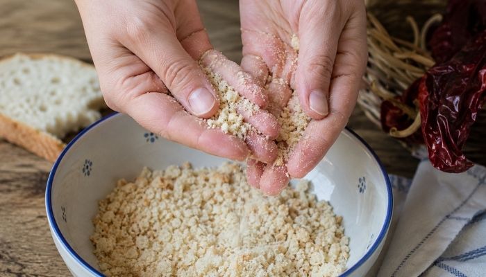 Mani che sbriciolano finemente la mollica di pane tra i palmi delle mani