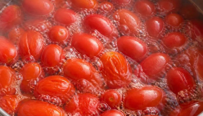 Primo piano pomodori rossi che bollono in acqua all'interno di una pentola