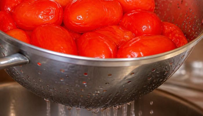 Pomodori rossi appena sbollentati in uno scolapasta metallico mentre l'acqua della bollitura scola attraverso i fori