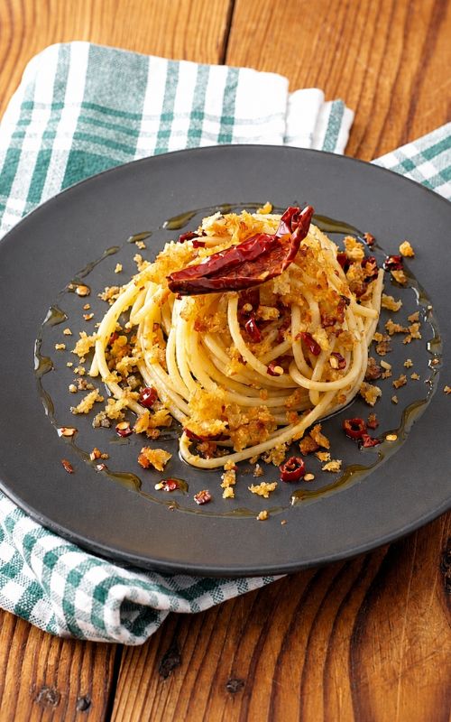 Spaghetti con peperone crusco e mollica croccante su piatto scuro foto verticale