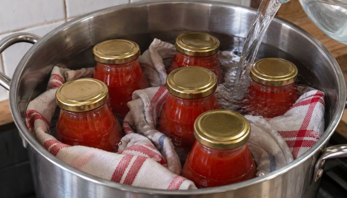 Bottiglie di vetro contenenti passata di pomodoro sistemate in un grande pentolone, separate da canovacci puliti mentre vengono coperte con acqua.