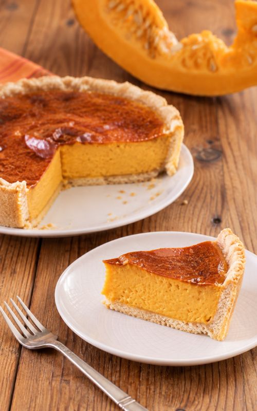 Fetta di crostata di zucca cremosa servita su un piatto, con una zucca fresca sullo sfondo